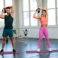 Para ćwiczy kettlebell. Kobieta i mężczyzna wykonują ćwiczenia z kettlebell nad głową, budując siłę.