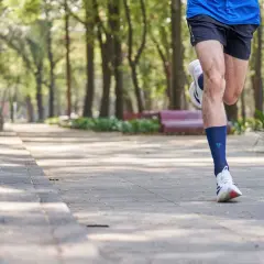 Mężczyzna biegnie po parku, wykonując liss cardio. W tle drzewa i ławki.