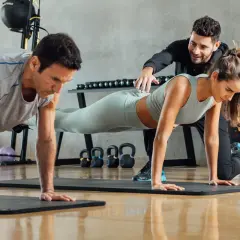 Trening funkcjonalny w praktyce: mężczyzna i kobieta wykonują pompki pod okiem trenera.