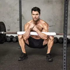 Mężczyzna wykonuje ćwiczenie zercher squat z gryfem opartym na przedramionach.
