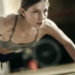 Kobieta w sportowym topie wykonuje pompki szwedzkie, skupiona na treningu.