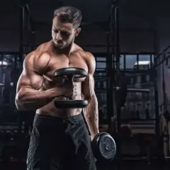 Mięśniowy mężczyzna ćwiczy biceps z hantlami. Zastanawia się, ile serii na plecy w tygodniu będzie optymalne dla jego treningu.