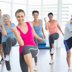 Uśmiechnięci ludzie w różnym wieku ćwiczą w sali gimnastycznej, wykonując ruchy inspirowane **les mills bodybalance**.