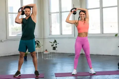 Para ćwiczy kettlebell. Kobieta i mężczyzna wykonują ćwiczenia z kettlebell nad głową, budując siłę.