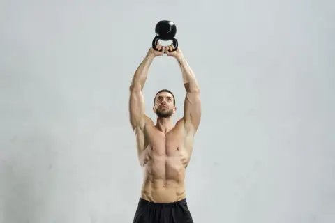 Mężczyzna wykonuje ćwiczenie z kettlebell. Kettlebell swing jakie mięśnie pracują? Mięśnie brzucha, pośladków i ud są mocno zaangażowane.