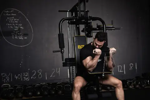 Mężczyzna ćwiczy biceps na maszynie. Różne rodzaje treningu siłowego są widoczne na tablicy i w tle.