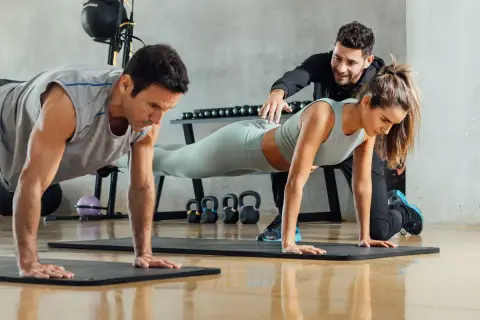 Trening funkcjonalny w praktyce: mężczyzna i kobieta wykonują pompki pod okiem trenera.