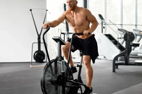 Mężczyzna ćwiczy na rowerze stacjonarnym po treningu siłowym. Zastanawia się, ile cardio jest optymalne.