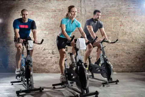 Trzy osoby ćwiczą na rowerach stacjonarnych. Intensywny trening spinningowy to świetny sposób na poprawę kondycji.