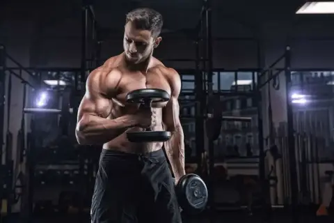 Mięśniowy mężczyzna ćwiczy biceps z hantlami. Zastanawia się, ile serii na plecy w tygodniu będzie optymalne dla jego treningu.