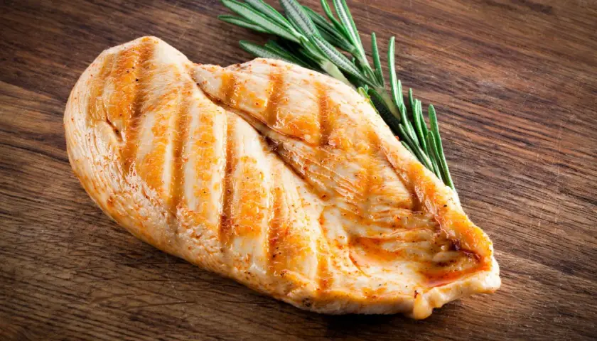 Grillowana pierś z kurczaka z rozmarynem na drewnianej desce. Dowiedz się, ile białka ma pierś z kurczaka.