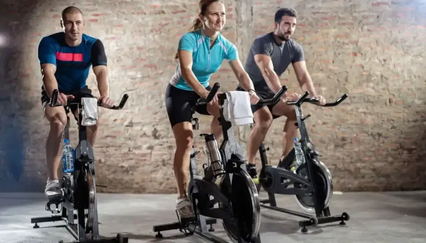 Trzy osoby ćwiczą na rowerach stacjonarnych. Intensywny trening spinningowy to świetny sposób na poprawę kondycji.
