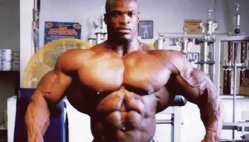 Ronnie Coleman dzisiaj, prezentuje imponującą muskulaturę. W tle widać trofea i wentylator.