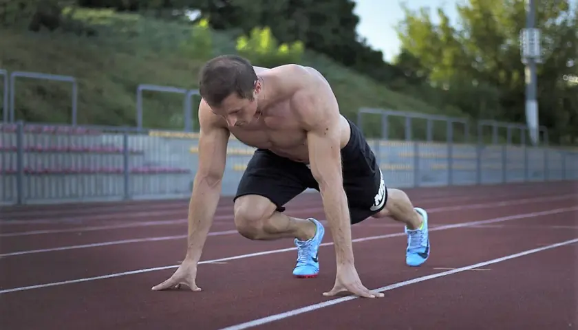 Mięśniowy sprinter w pozycji startowej na bieżni. Intensywny trening sprinterski w pełni.