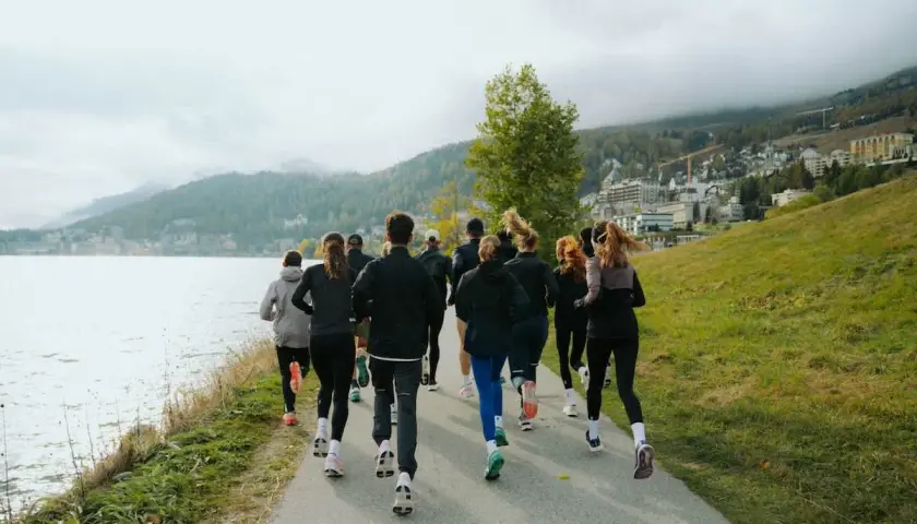 Grupa biegaczy w malowniczej scenerii nad jeziorem. Widok z tyłu na ludzi w sportowych strojach, którzy biegną ścieżką. To inspiracja, jak polubić bieganie.
