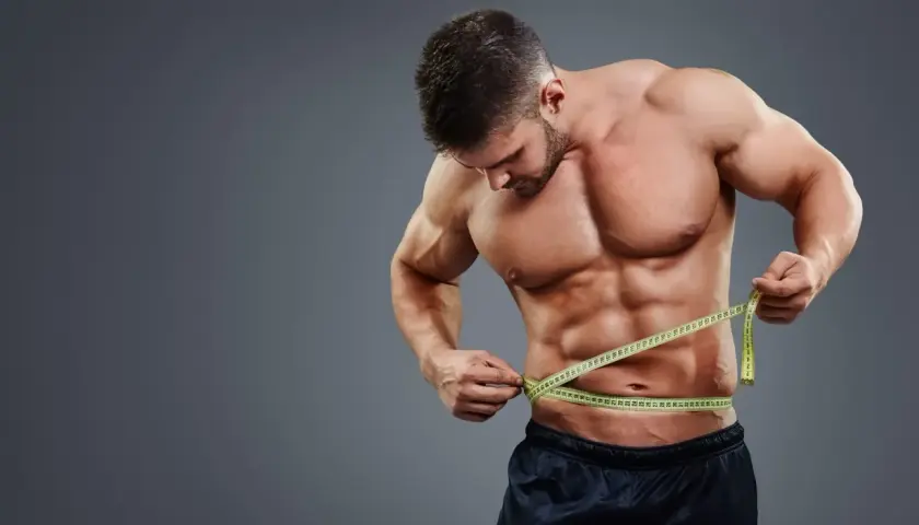Mężczyzna z wyrzeźbionym brzuchem mierzy talię centymetrem, kontrolując efekty lean bulk.