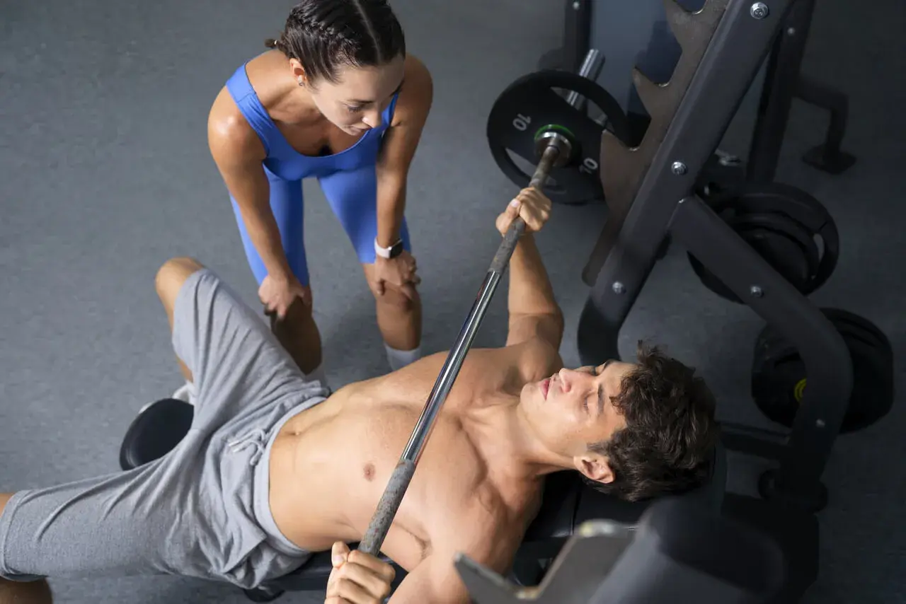 Trening pull: mężczyzna ćwiczy klatkę piersiową na ławce, kobieta asekuruje.