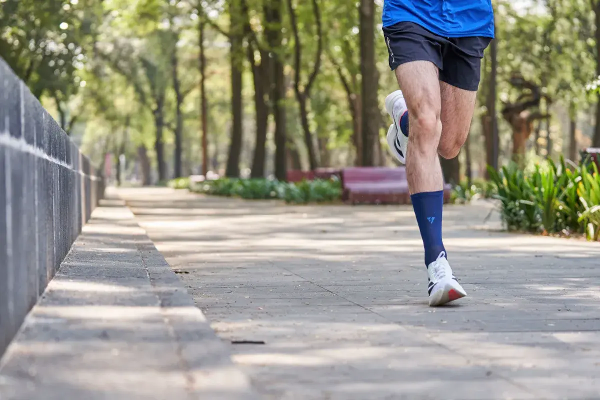 Mężczyzna biegnie po parku, wykonując liss cardio. W tle drzewa i ławki.