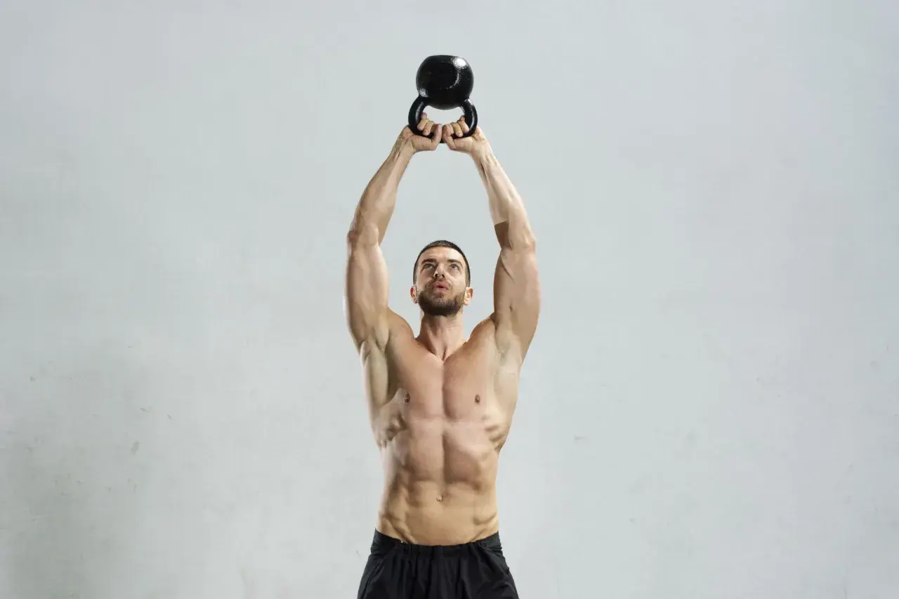 Mężczyzna wykonuje ćwiczenie z kettlebell. Kettlebell swing jakie mięśnie pracują? Mięśnie brzucha, pośladków i ud są mocno zaangażowane.