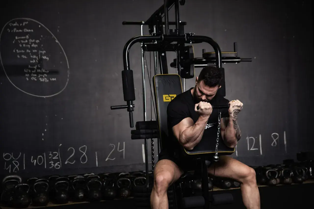 Mężczyzna ćwiczy biceps na maszynie. Różne rodzaje treningu siłowego są widoczne na tablicy i w tle.