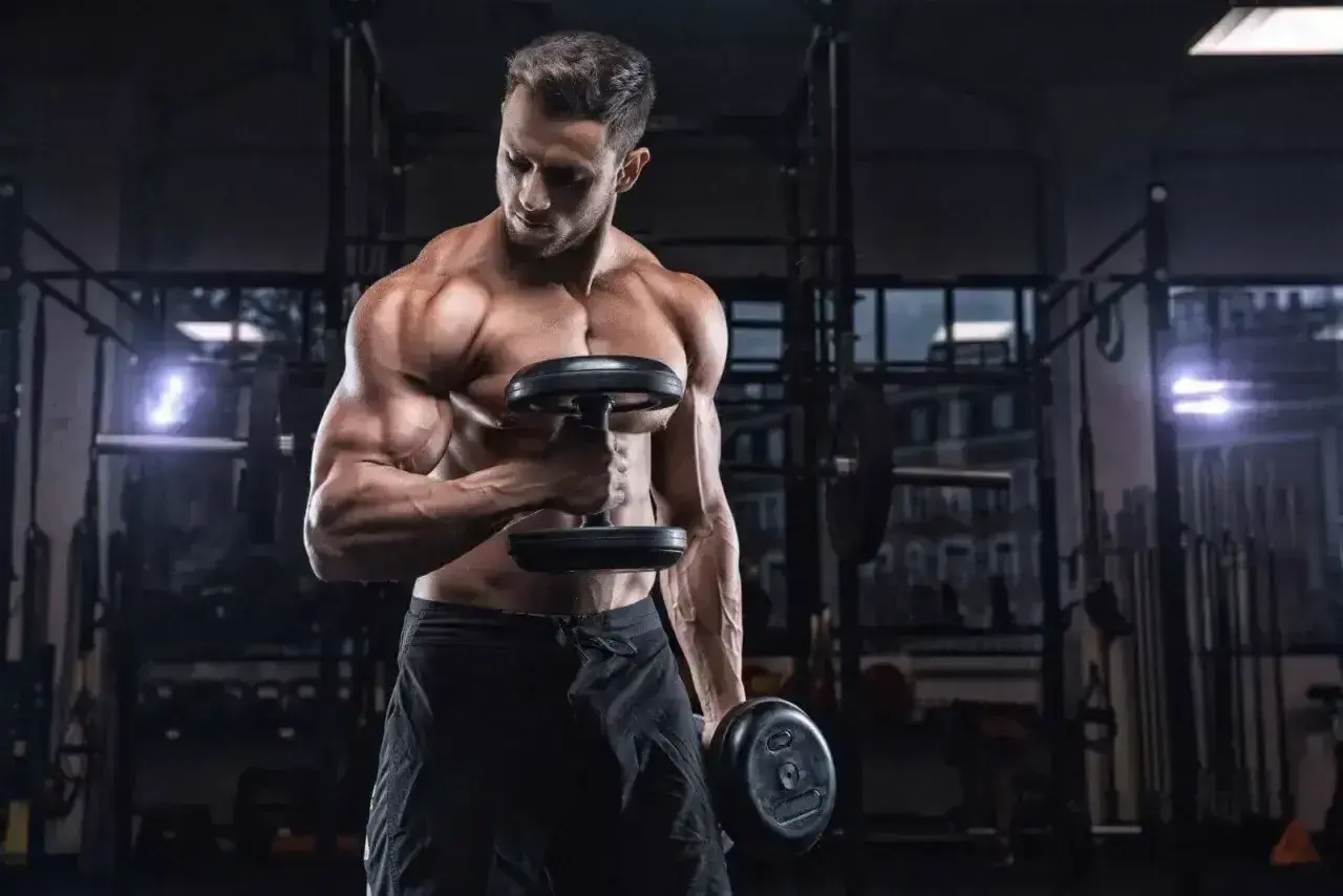 Mięśniowy mężczyzna ćwiczy biceps z hantlami. Zastanawia się, ile serii na plecy w tygodniu będzie optymalne dla jego treningu.