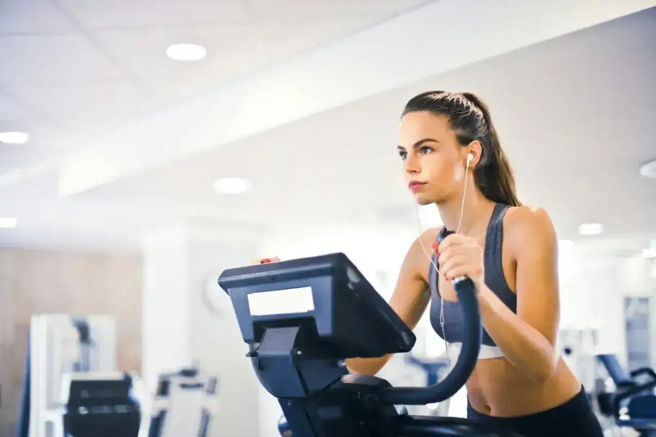 Kobieta ćwiczy na orbitreku, słuchając muzyki. Zastanawia się, ile cardio po treningu siłowym będzie optymalne.