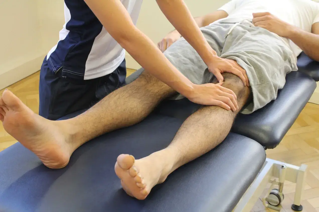 Fizjoterapeuta wykonuje ćwiczenia na kolano z chondromalacją rzepki, pomagając pacjentowi w rehabilitacji.