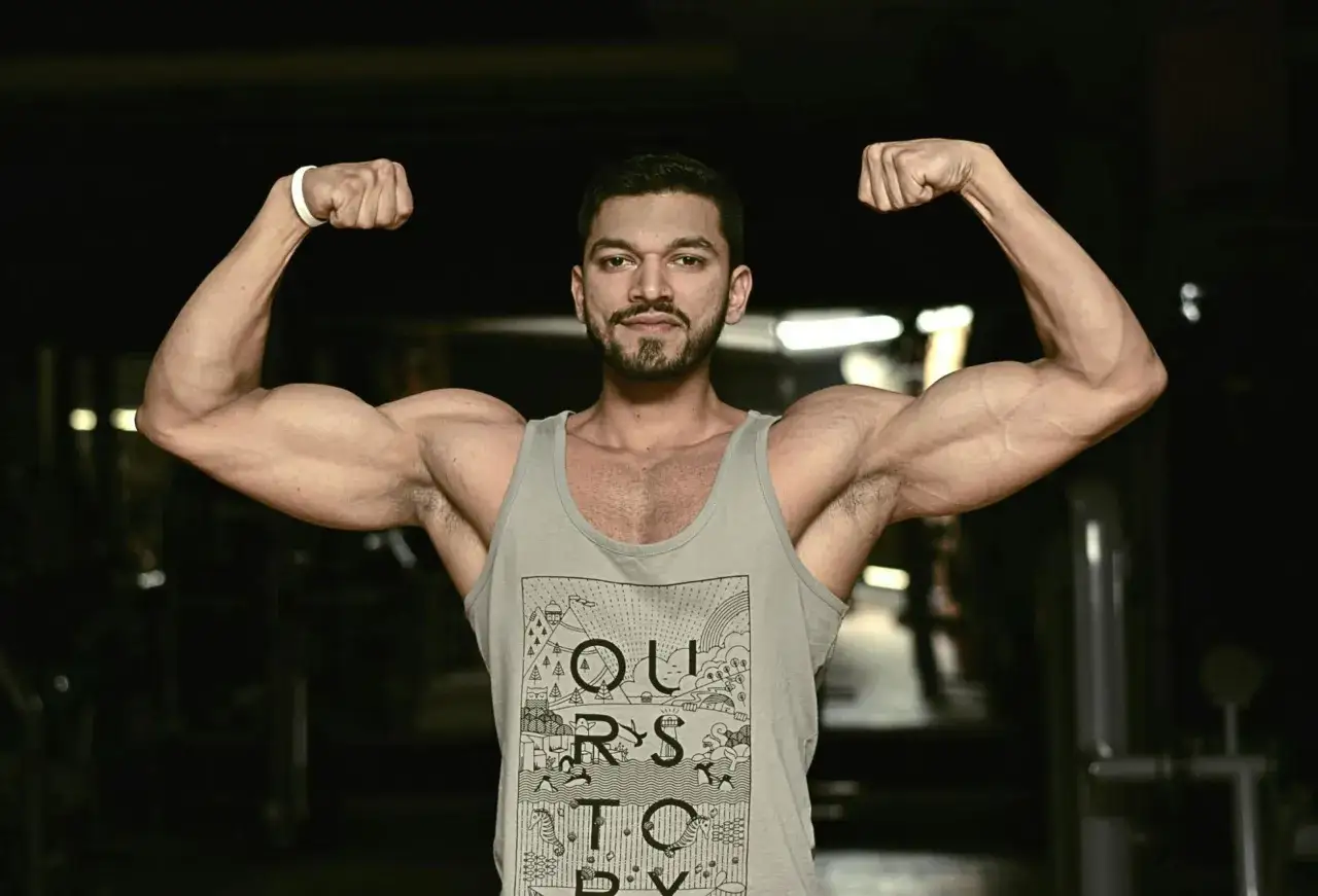 Mężczyzna z brodą prezentuje swój duży biceps, napinając mięśnie w siłowni.