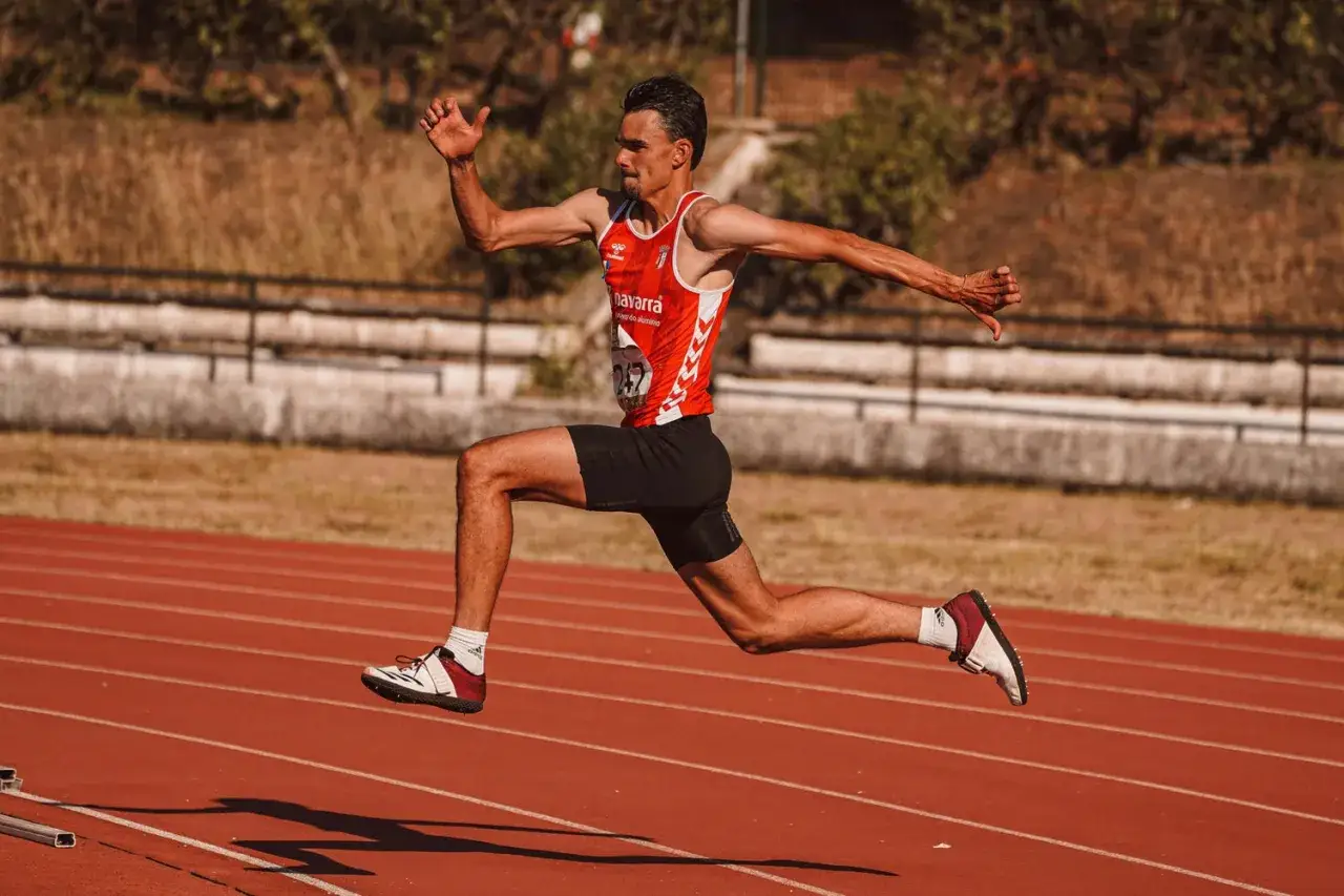 Sprinter w czerwonej koszulce i czarnych spodenkach demonstruje siłę biegową, unosząc się w powietrzu na bieżni.