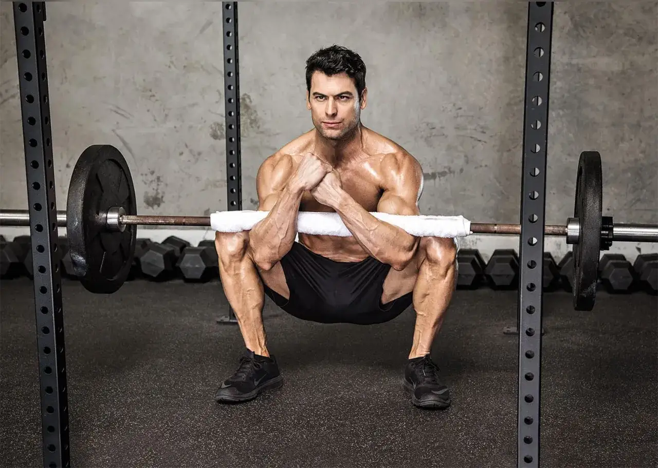 Mężczyzna wykonuje ćwiczenie zercher squat z gryfem owiniętym ręcznikiem.