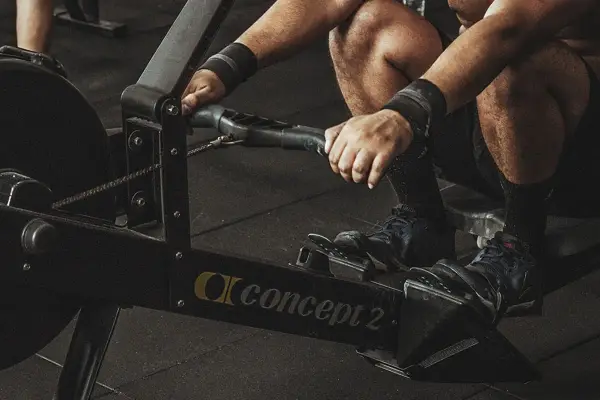 Intensywny trening na ergometrze wioślarskim. Widoczne dłonie z opaskami, nogi w butach sportowych i maszyna Concept 2. To świetne efekty dla całego ciała.