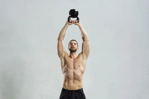 Mężczyzna wykonuje ćwiczenie z kettlebell. Kettlebell swing jakie mięśnie pracują? Mięśnie brzucha, pośladków i ud są mocno zaangażowane.