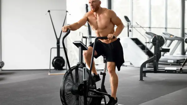 Mężczyzna ćwiczy na rowerze stacjonarnym po treningu siłowym. Zastanawia się, ile cardio jest optymalne.